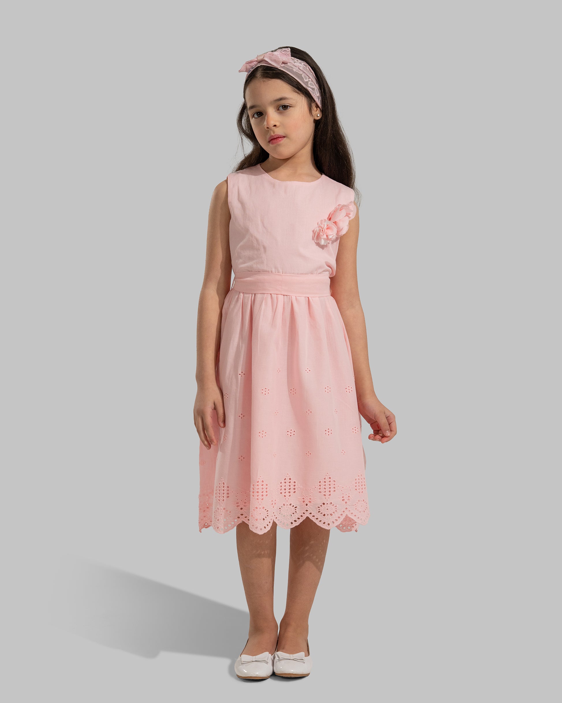 sleeveless pink cotton eyelet dress featuring a floral appliqué on the chest and a matching waist belt.