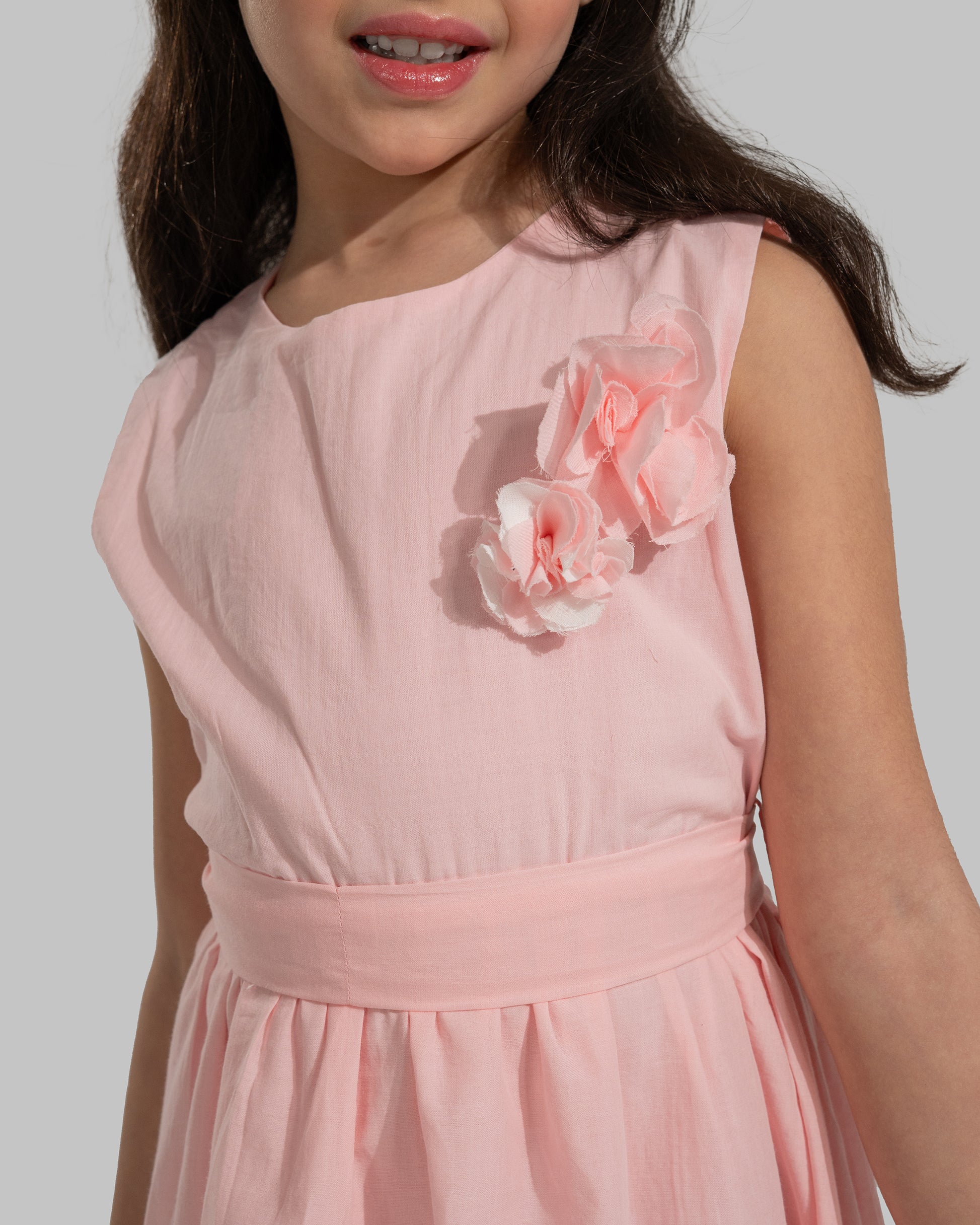 sleeveless pink cotton eyelet dress featuring a floral appliqué on the chest and a matching waist belt.