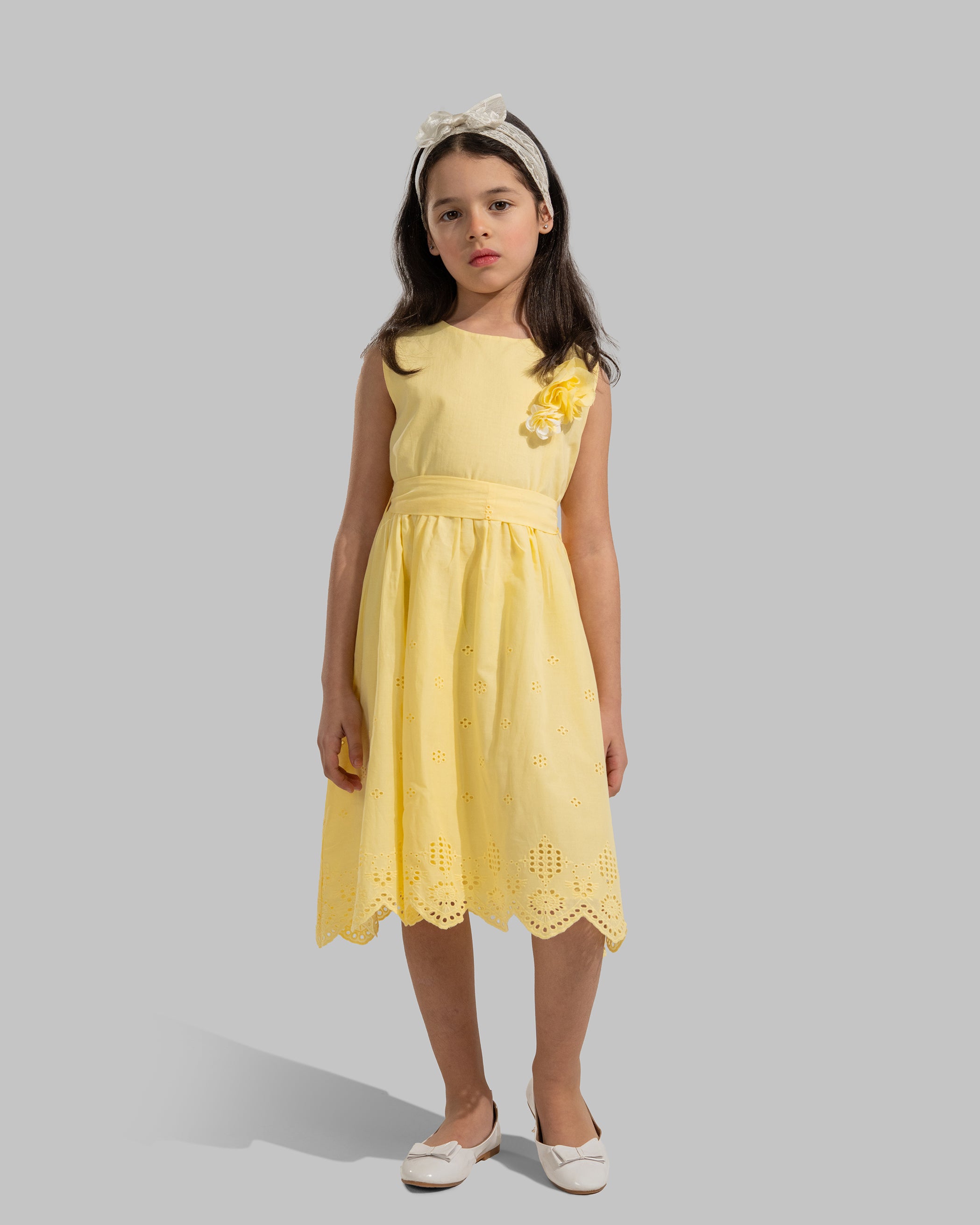 sleeveless pink cotton eyelet dress featuring a floral appliqué on the chest and a matching waist belt.